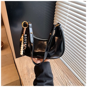 Detail of black patent leather hobo bag with wooden beads and fashion lettering