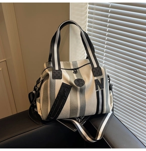 Detail view of striped canvas tote bag showing side zipper pocket and letter N patch