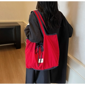 Detail of red canvas tote bag featuring navy trim and decorative bow on the handle