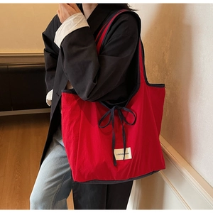 Detail of red canvas tote bag with blue trim and bow knot carried by a model