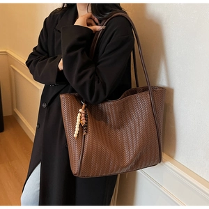 Detail of dark brown woven tote bag with beaded pendant and long shoulder strap