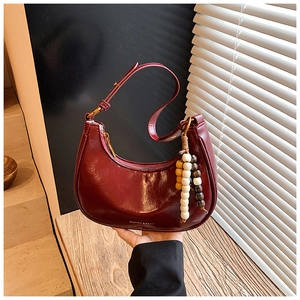 Detail of burgundy hobo bag with glossy leather finish and unique wooden bead charm