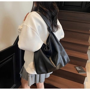Detail of a black leather slouchy tote bag with knotted strap shown on model's shoulder