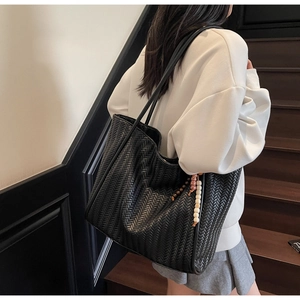 Detail of black woven tote bag with bohemian beaded charm and intricate leather texture