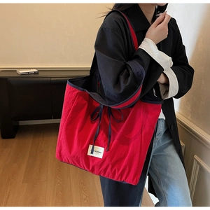 Detail of red nylon tote bag with blue straps and Late Morning brand patch logo
