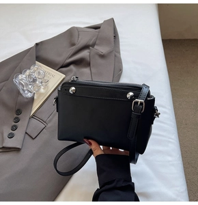 Detailansicht einer schwarzen Ledertasche mit silbernen Nieten auf einem grauen Sakko
