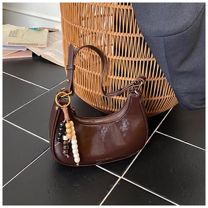 Detail of dark brown glossy hobo bag with wood bead charm on leather shoulder strap
