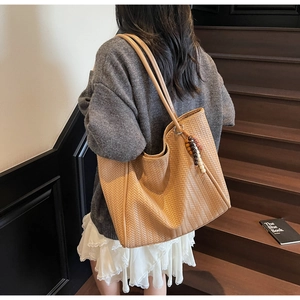 Close-up of caramel woven tote bag with wooden beads detail on a model's shoulder