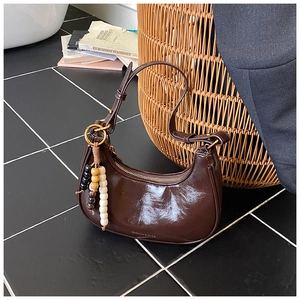 Detail of a dark brown glossy patent leather crescent bag with beaded charm and logo