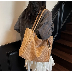 Close-up of woven large tote bag in light brown with decorative bead charm detail