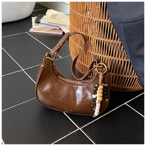Detail shot of brown crescent bag with retro wooden bead tassel on tile floor