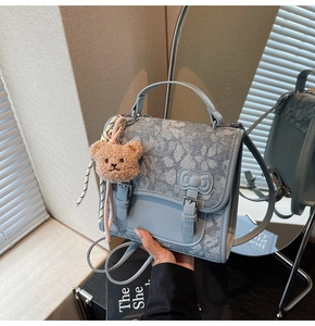 Detail of light blue denim floral backpack with bow buckles and plush bear charm