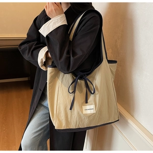 Detail of beige tote bag with blue trim and side drawstring bow on a shoulder strap