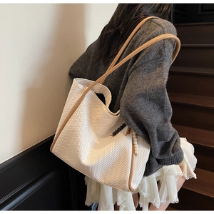 Detail of white woven tote bag with brown leather straps and beaded tassel charm accessory