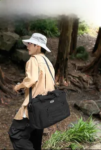 Close-up of black tactical canvas travel bag with wide shoulder strap in outdoor forest