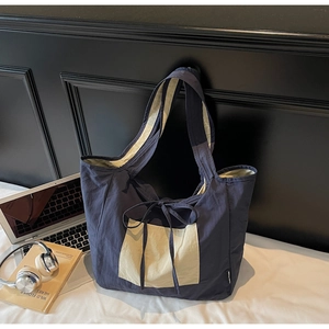 Detail of navy blue tote bag with cream pocket and bow tie in a stylish workspace setup