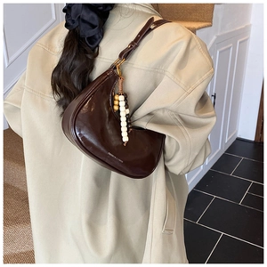 Detail of a dark brown half-moon underarm bag in shiny faux leather with wooden bead charm