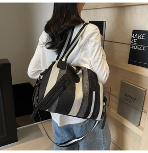 Detail of striped canvas tote bag showing front zipper pocket and logo on model