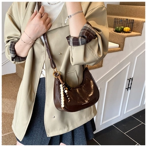 Detail of dark brown glossy crescent bag with wooden bead charm and leather strap
