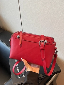 Rote Leder-Umhängetasche mit silbernen Beschlägen und verstellbarem Gurt in der Hand