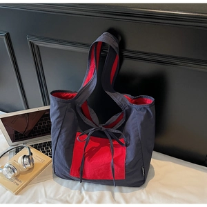 Detail of red and blue nylon tote bag with bow accent next to laptop and headphones