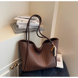 Detail of dark brown woven tote bag featuring V-shaped texture and a beaded tassel charm