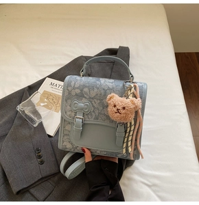 Detail of light blue floral jacquard handbag with brown plush bear charm and dual buckles