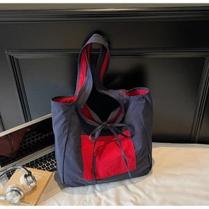 Detail view of canvas tote bag with contrast red pocket and decorative ribbon ties