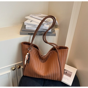 Macro detail of brown woven tote bag featuring leather texture and beaded charm