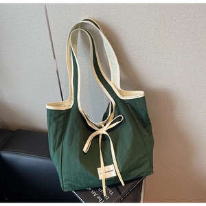Close-up of dark green tote bag featuring ivory trim and decorative bow accent