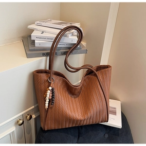 Close-up of brown woven tote bag featuring vintage bead charm and herringbone texture