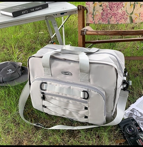 Detailed view of light grey travel duffel bag with bungee storage on outdoor lawn