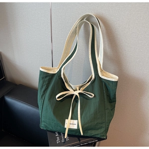 Detail of dark green tote bag with beige trim and bow against a black leather sofa
