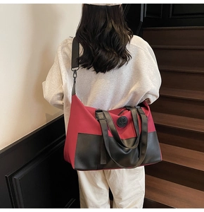 Detail of red and black large travel bag with adjustable strap and logo on wooden stairs