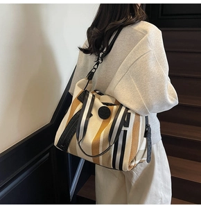 Detailed side view of the striped canvas tote bag worn by a model on a shoulder strap