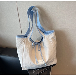 Detail of minimalist cream tote bag featuring light blue bow closure and brand fabric label