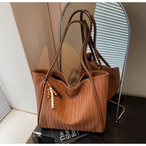 Detail of woven caramel leather tote bag with wooden bead charm in a minimalist home setting