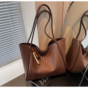 Detail of dark brown woven tote bag with beads charm and minimalist leather straps