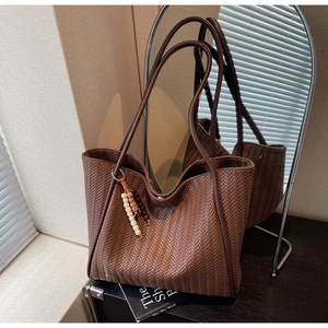 Detail of brown herringbone woven tote bag with beaded charm on wooden surface