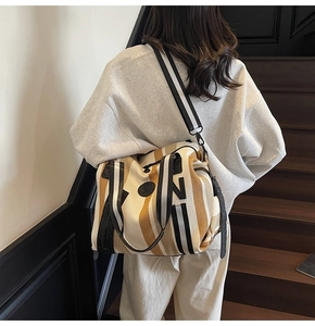 Detail of striped canvas tote bag with leather logo and removable shoulder strap worn by model