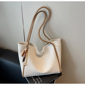 Detailed woven texture of off-white tote bag with beaded tassel charm and brown straps