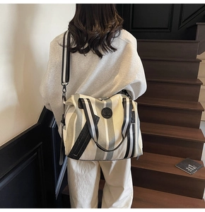 Rear view of striped canvas tote bag with black straps on a female model in an indoor setting