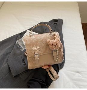 Detail of cream floral backpack with decorative bow and plush bear charm on a grey blazer