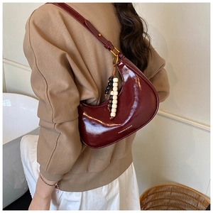 Detail view of burgundy moon bag with glossy patent leather finish and beaded charm decoration