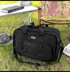 Outdoor camping scene showing large black travel duffel bag with NOCOBAG logo on grass