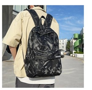 Rear view of model wearing a black camouflage waterproof backpack on a sunny street