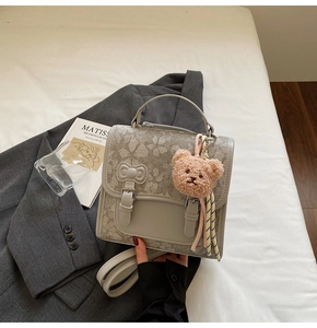 Detail of light gray crossbody bag with clover prints, bow accent, and cute bear charm