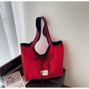 Detail view of a large red tote bag with bow drawstring on a desk with a laptop