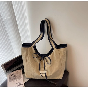 Close-up of khaki nylon tote bag with navy trim and decorative bow on a leather bench
