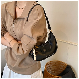 Detail of black crescent bag with glossy patent leather finish and beaded charm detail